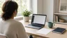Person at a home desk with a laptop and a printed note beside it